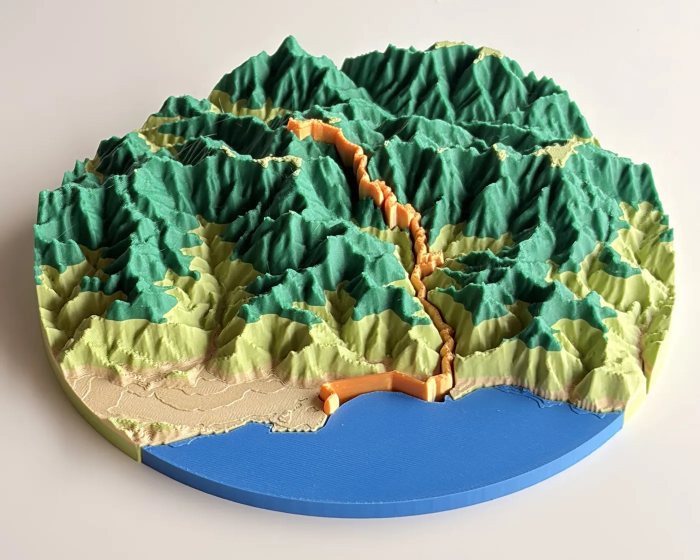Un mapa de carrera real impreso en 3D de la Taiwan KOM Challenge hecho con TrailMark3D: una pieza circular con el recorrido de la carrera ciclista en relieve naranja, desde el mar azul hasta las montañas verdes